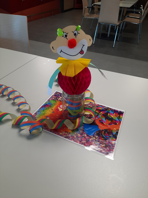 Papierclown steht auf einem Tisch, umgeben von bunten Feierdekorationen.