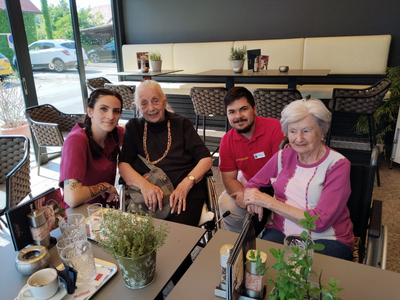 Vier Personen, darunter älteren Frauen, sitzen in einem Café am Tisch.
