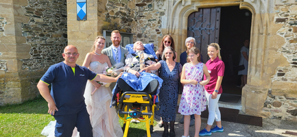 Eine Hochzeitsgruppe mit einem Rollstuhlpatienten vor einer Kirche.
