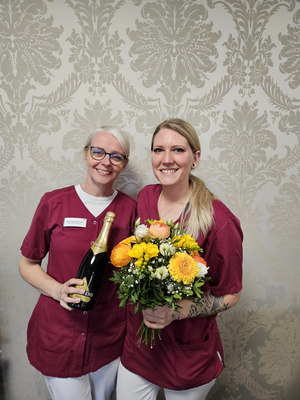 Zwei Frauen in Uniform halten Sekt und einen bunten Blumenstrauß.