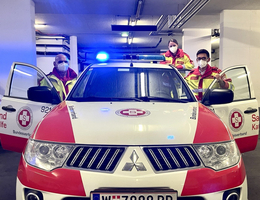 zwei Rettungssanitäterinnen mit Maske, bei Rettungsauto, geöffnete Türen, stehen dahinter 