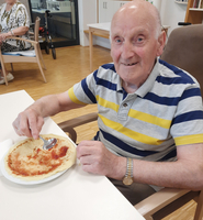 Ein älterer Mann sitzt am Tisch und isst einen Pfannkuchen mit Sauce.