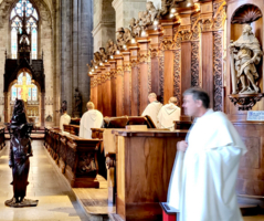 Männer in weißen Gewändern stehen in einer Kirche, Holzverarbeitung im Hintergrund.