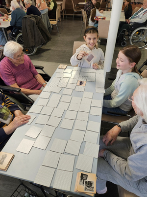 Zwei Kinder spielen Memory mit älteren Menschen an einem Tisch.
