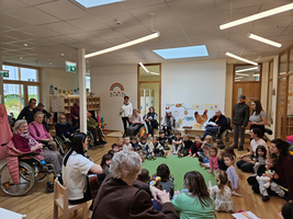 Senioren und Kinder sitzen gemeinsam in einem Raum, lauschen einer Darbietung.