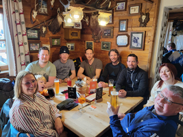 Gruppe von acht Personen sitzt an einem Tisch in einer gemütlichen Berghütte.
