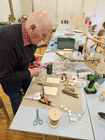 Ein älterer Mann bastelt mit Holz und Materialien an einem Tisch.