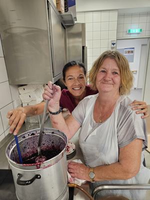 Zwei Frauen rühren gemeinsam in einem großen Topf mit einer dunklen Masse.