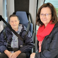Ein älterer Mann und eine Frau sitzen in einem Fahrzeug.