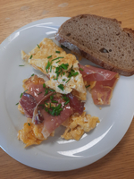 Ein Teller mit Rührei, Schinken und einem Stück Vollkornbrot.