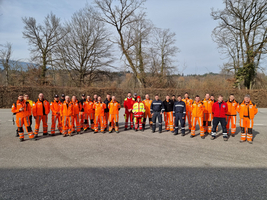 Gruppenaufnahme Personen in orangenen Uniformen, daziwschen Personen in roten Samariterbund Uniformen, im Hintergrund kahle Bäume