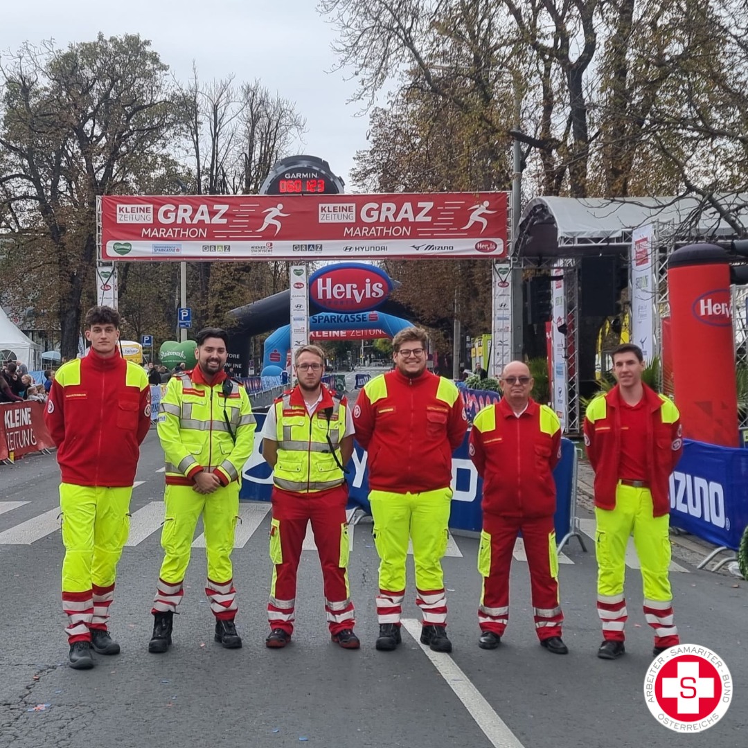 Sechs Rettungskräfte in leuchtenden Uniformen stehen am Ziel des Graz Marathons.